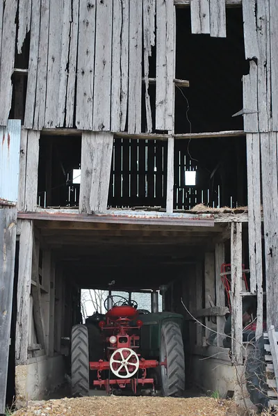 Red tractor parked inside a weathered wooden barn