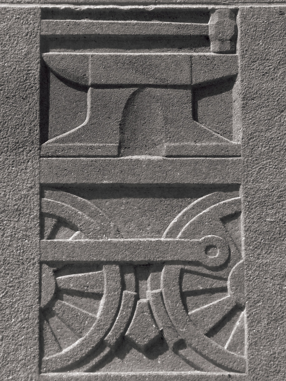 Relief carving of an anvil and locomotive wheels with coupling rod — historic image
