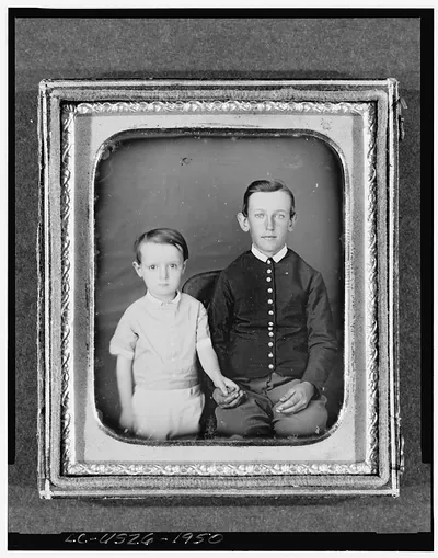 [Unidentified boy seated in chair with child standing to left, three-quarter length, facing front]