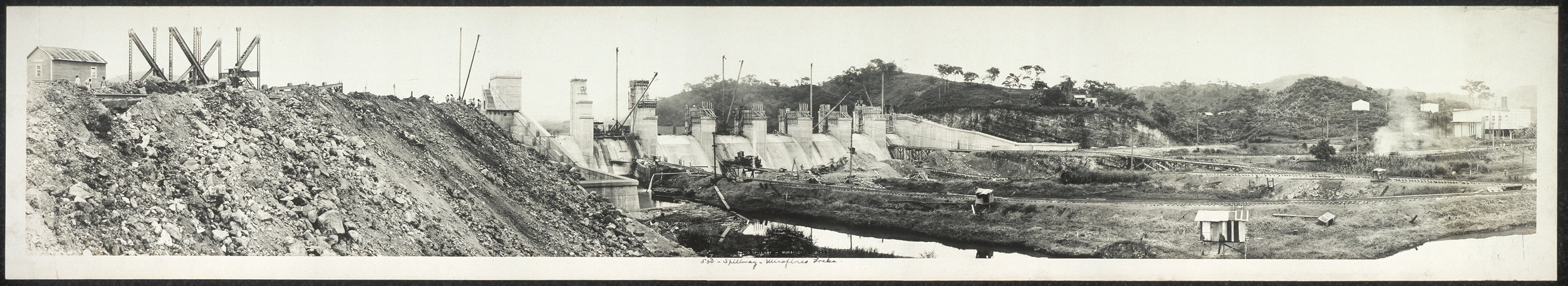 Concrete spillway under construction beside a rocky spoil heap — historic image