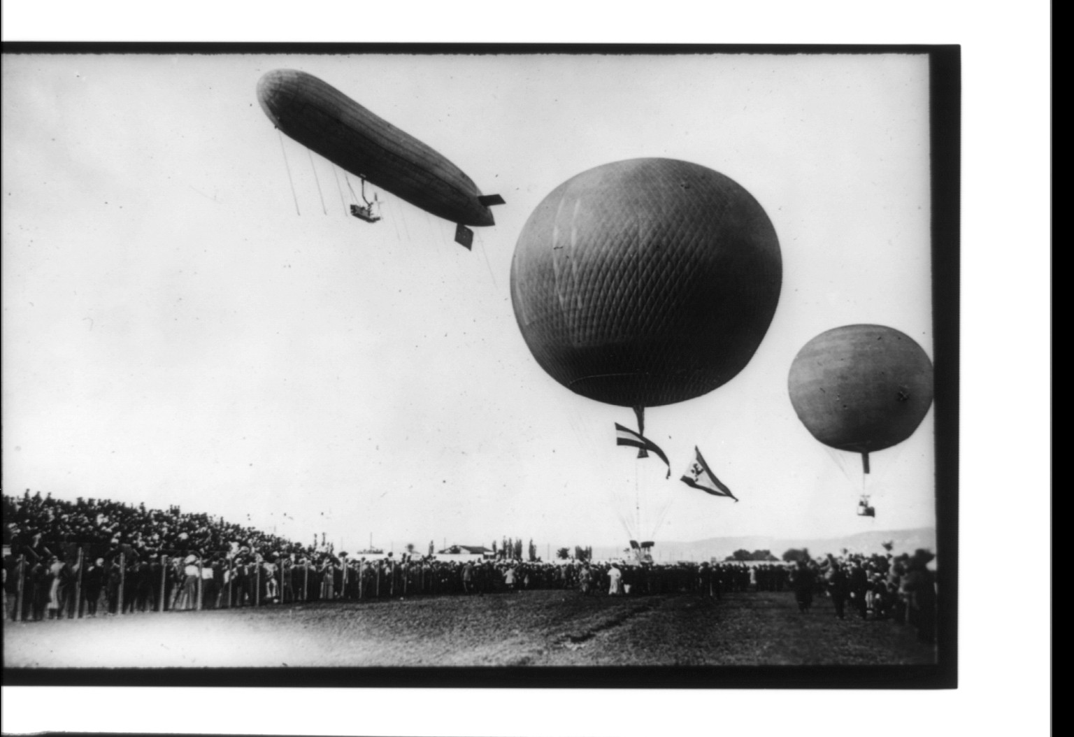 Dirigible and 2 balloons aloft above crowd, [ca. 1906] — historic image