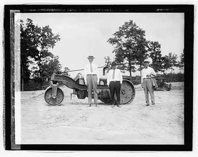 Three men standing beside a road roller on bare ground