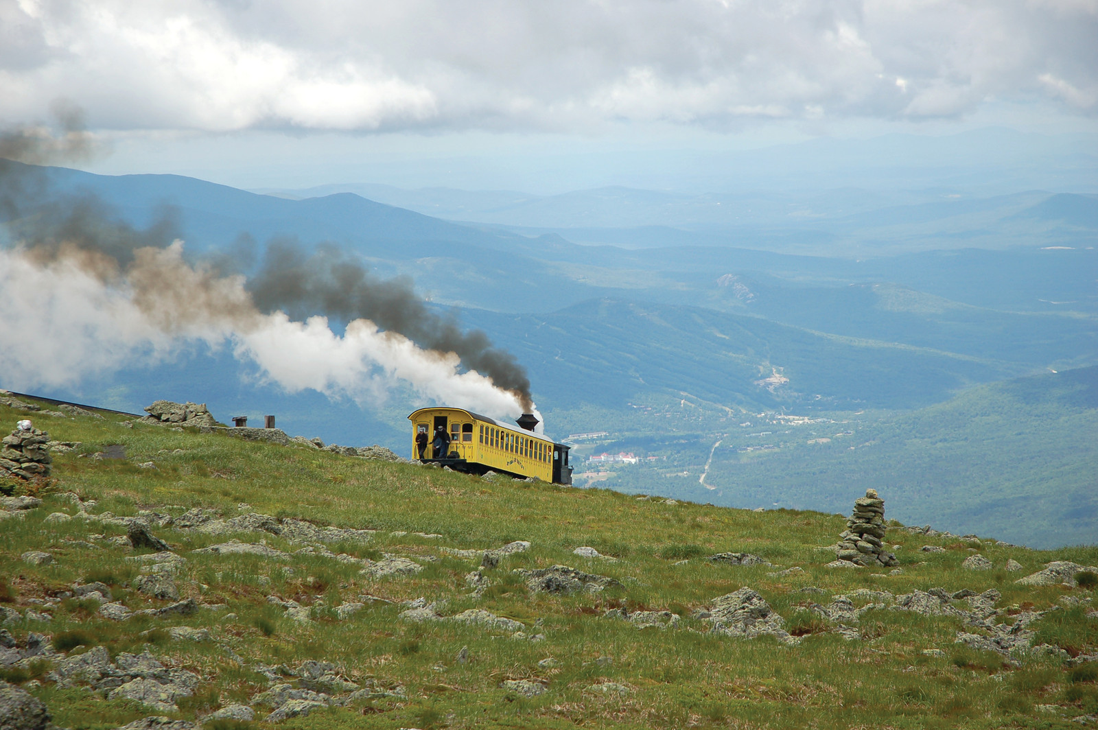 Yellow mountain cog railway car emitting steam over green slopes — historic image