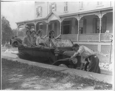 [Man cranking auto with five women, in front of The Mt. Arlington hotel]