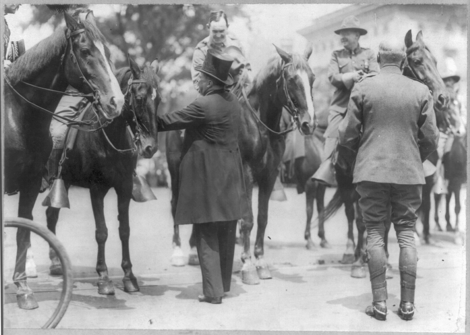 [Theodore Roosevelt, full length, standing, greeting Rough Riders on horseback, rear view] — historic photograph