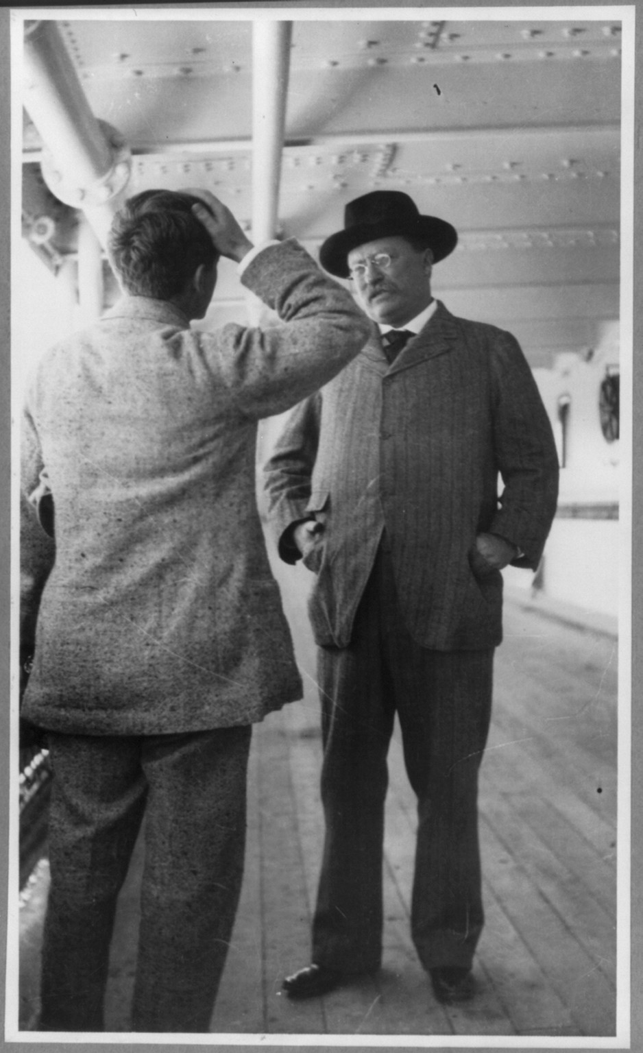 [Theodore Roosevelt, full length, standing with hands in coat pockets, facing left, talking with G. Gardner on the KAISERIN AUGUSTE VICTORIA] — historic photograph