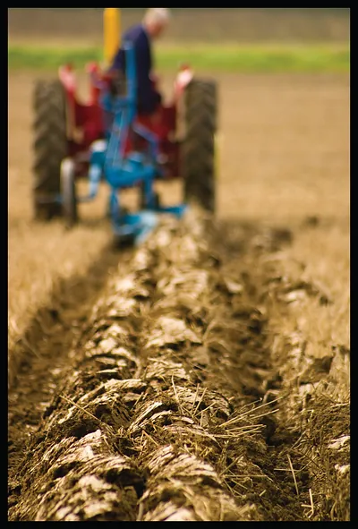 Tractor ploughing a field, driver seen from behind