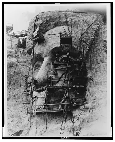 [Closeup of workmen carving the head of Abraham Lincoln on the granite face of Mount Rushmore]