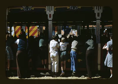 Crowd watching a fair game booth with striped canopy
