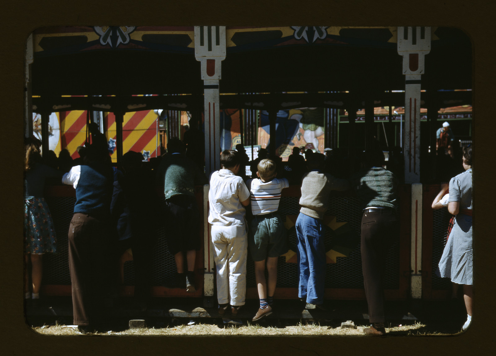 Crowd watching a fair game booth with striped canopy — historic image