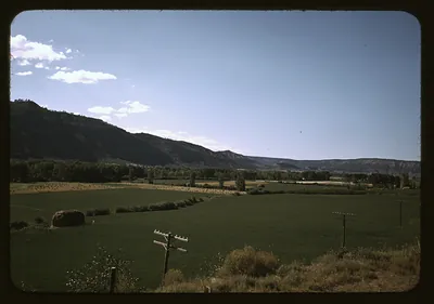 Irrigated green fields and hay bale below a mesa