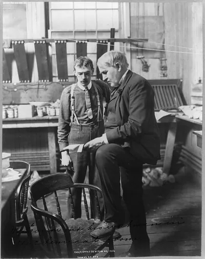 [Thomas Alva Edison, 1847-1931, full-length portrait, standing, facing left, with his workman in the chemical room]