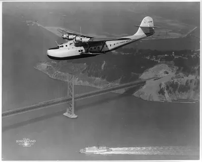 [Aerial view of Pan American Airways Philippine Martin Clipper ship in flight over San Francisco-Oakland Bay Bridge]