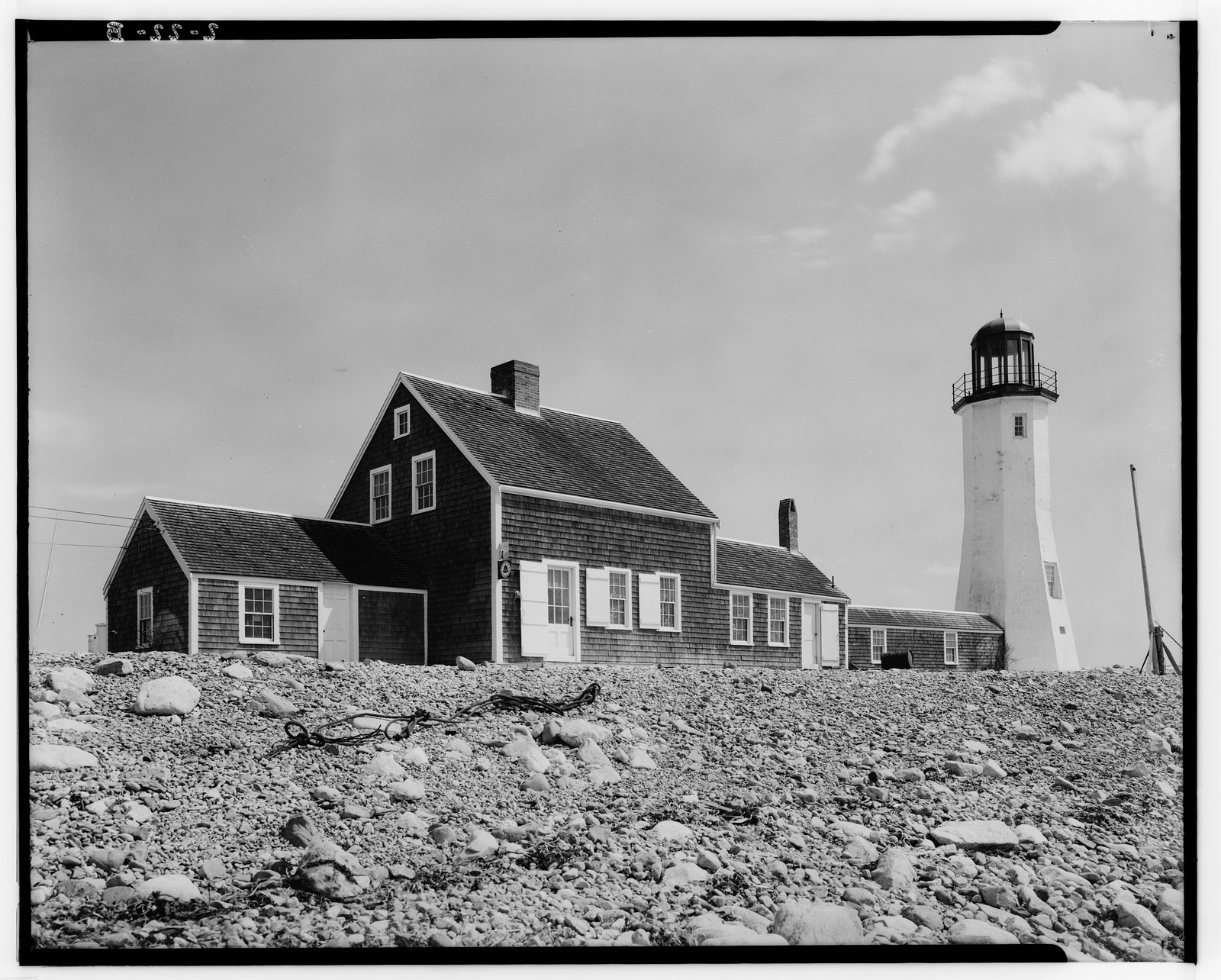 Shingled keeper's house and lighthouse on a rocky shore — historic image
