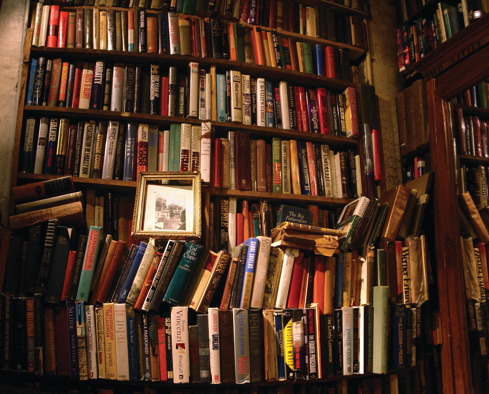 Crowded bookshelves with a gilt-framed picture among old books — historic image