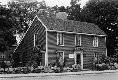 Colonial wooden house with stone wall, black and white photograph