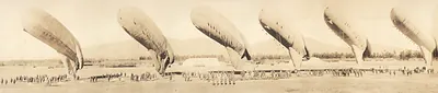 Several airships being inspected on a field before a crowd