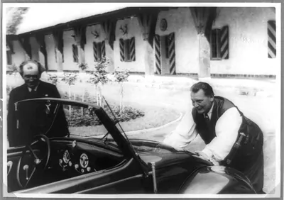 [Hermann Goering leaning on front of Volkswagen convertible given to him, Ferdinand Porsche looking on]