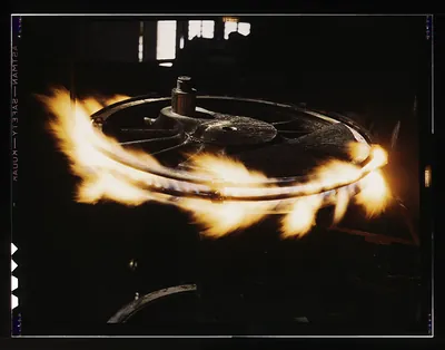 Flames burning around a spoked metal wheel in a dark workshop