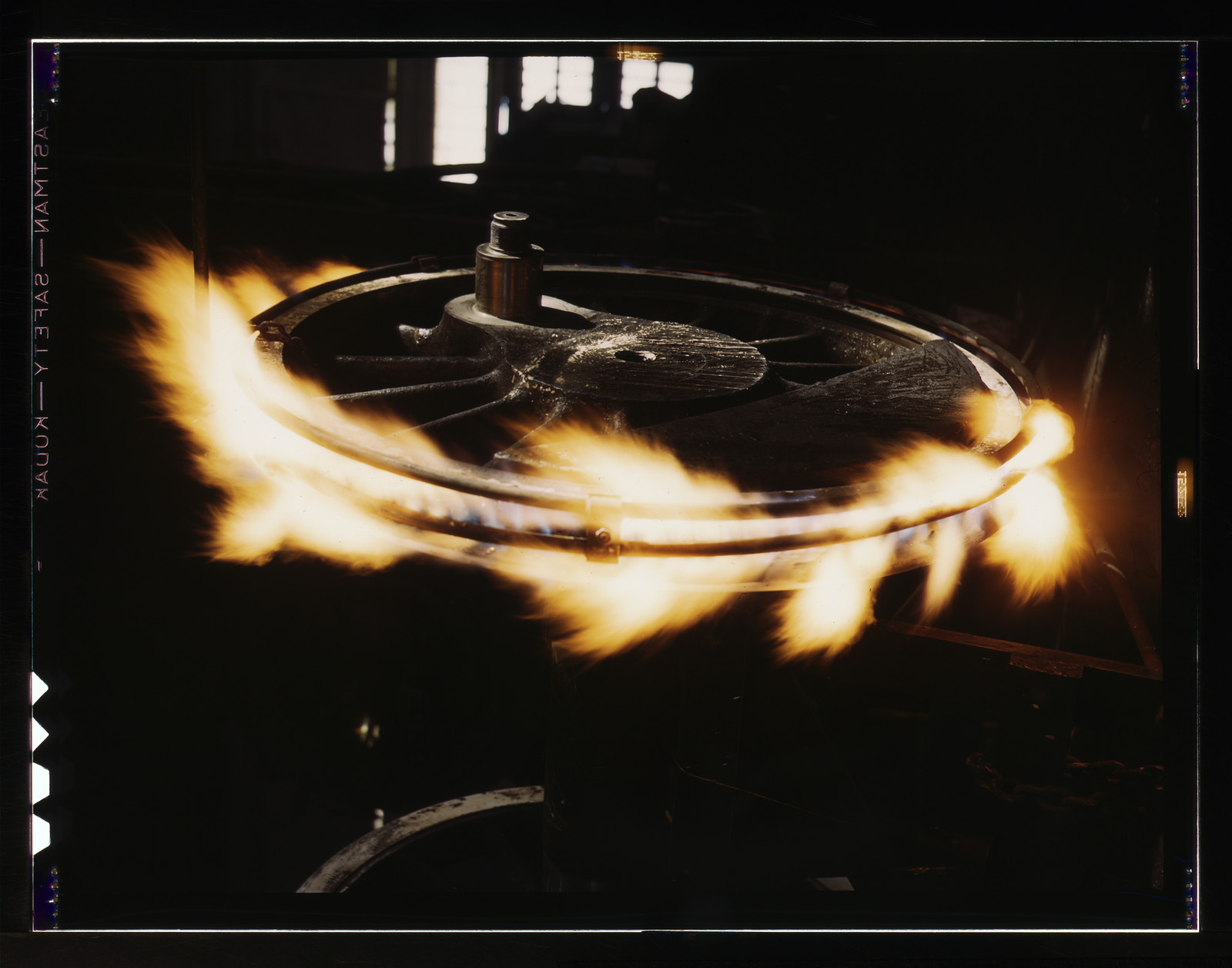 Flames burning around a spoked metal wheel in a dark workshop — historic image