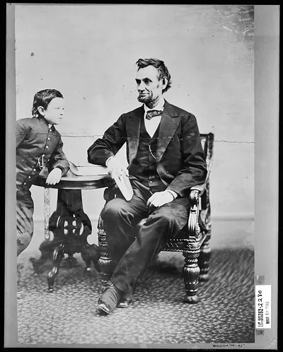 [Abraham Lincoln, seated and holding a book, with his son Tad (Thomas) leaning on a table]