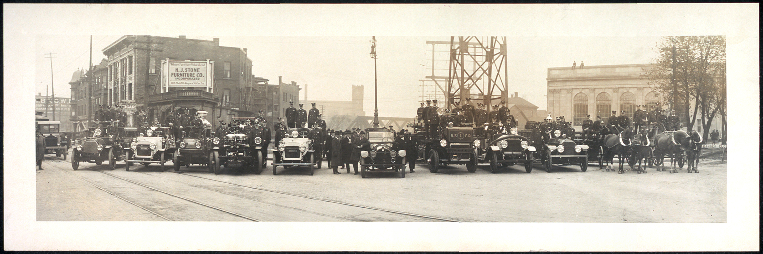 Firemen with vintage cars and horse-drawn apparatus on a city street — historic image