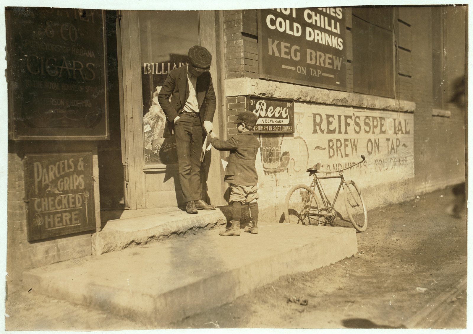 Boy handing item to man outside shop with bicycle — historic image