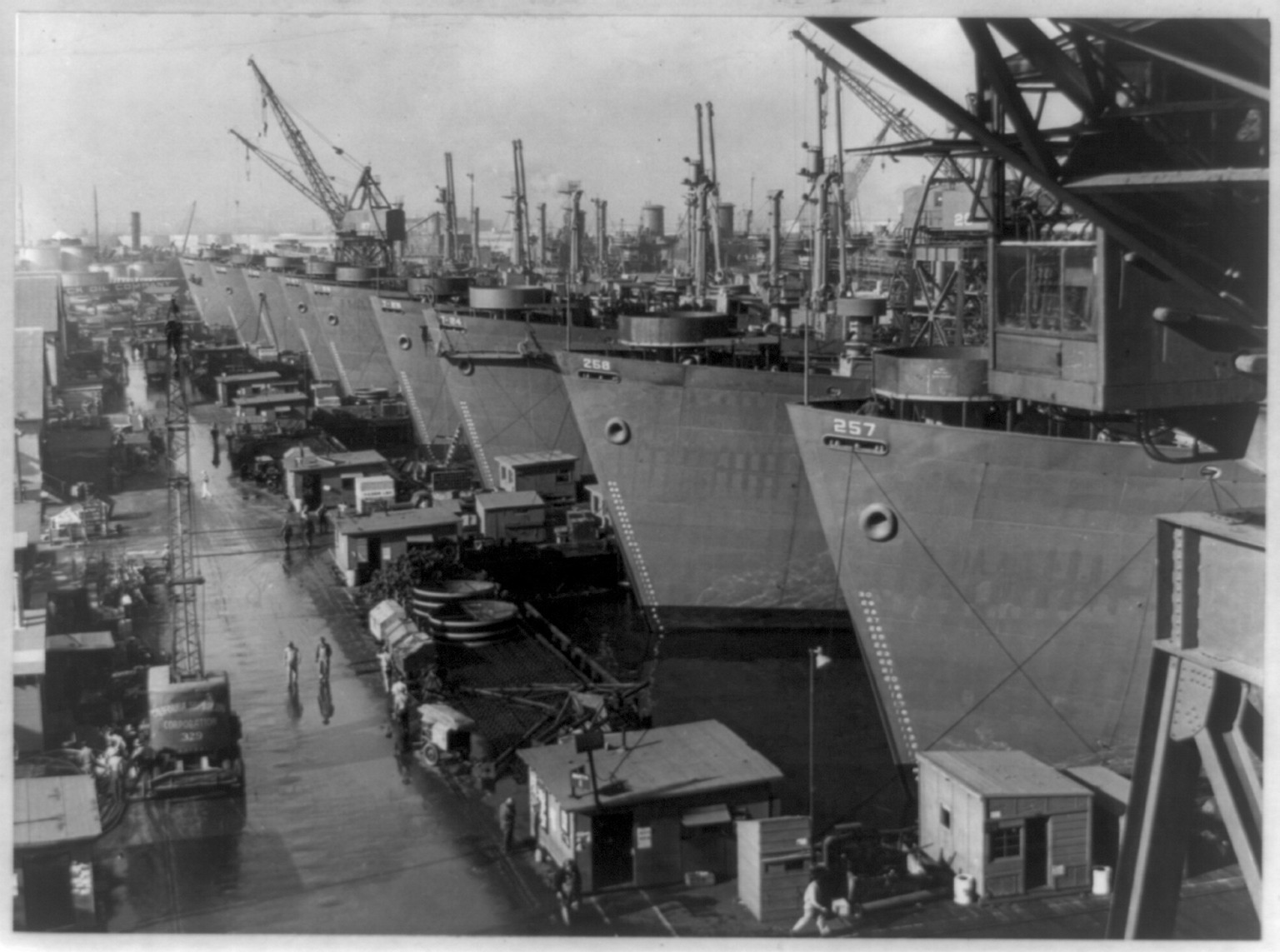 [Nine huge Liberty cargo ships at outfitting docks of California Shipbuilding Corporation's Los Angeles yards, nearly ready to be delivered to the U.S. Maritime Commission], 1943 Dec. 4. — historic photograph