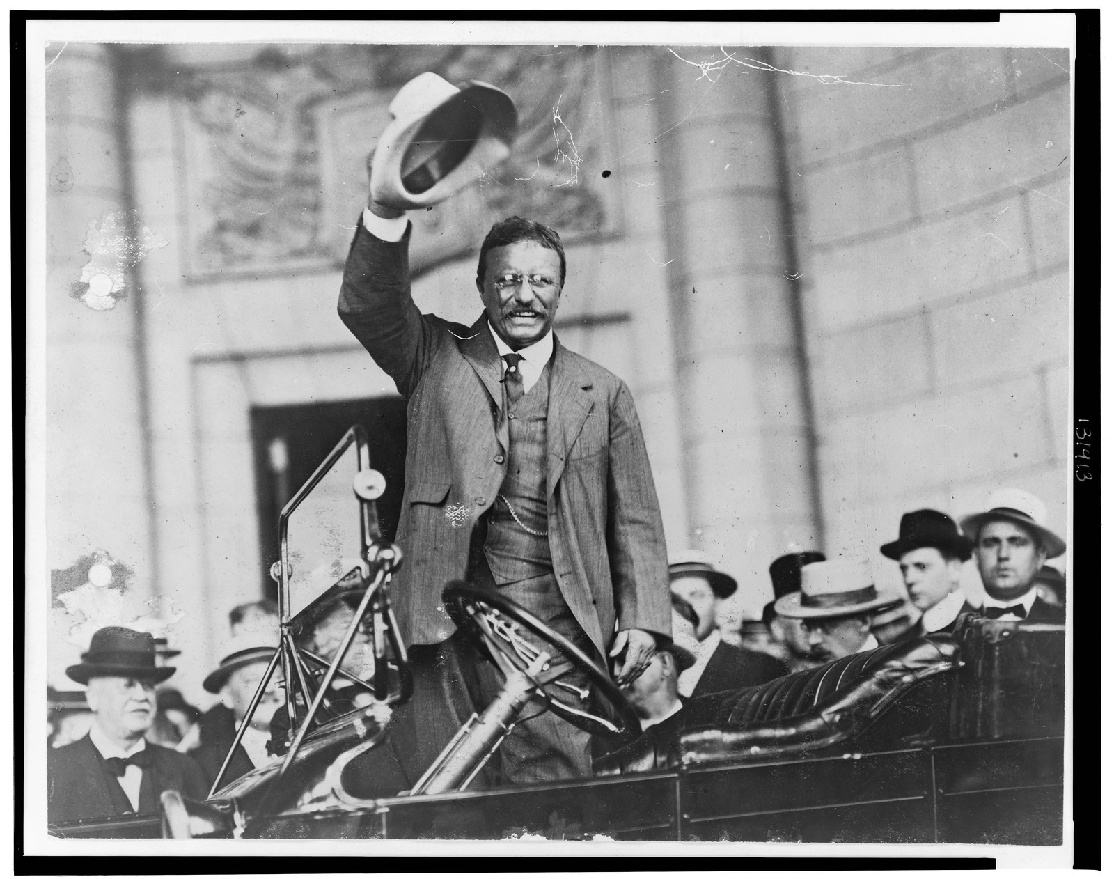 [Theodore Roosevelt, three-quarter length portrait, standing up in car, waving hat], [between 1909 and 1932] — historic photograph