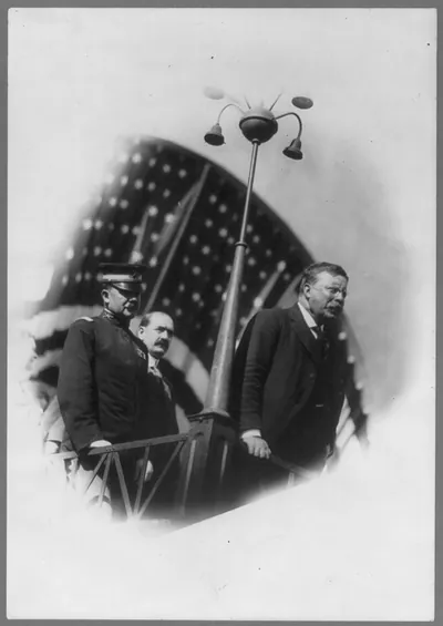 [Theodore Roosevelt, half length, speaking, facing right, with others behind him]