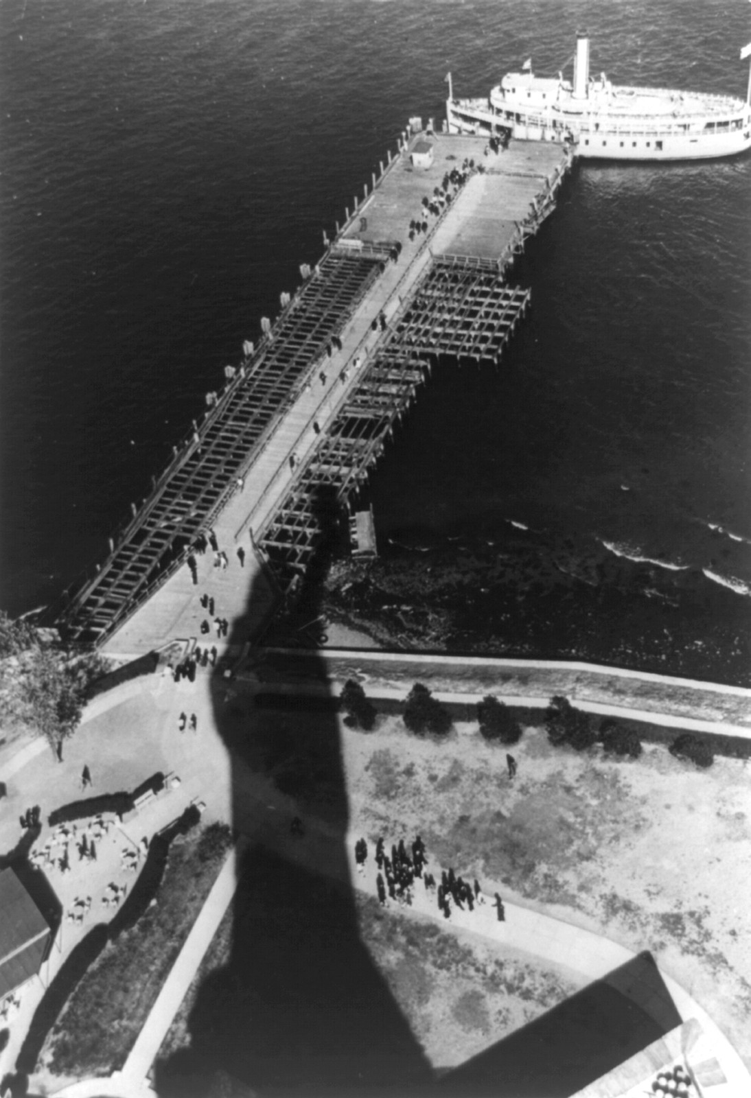 [View from Statue of Liberty of visitors walking beneath the raised right hand of the statue which casts a shadow on Bedloe's Island in New York Harbor], 1944 — historic photograph