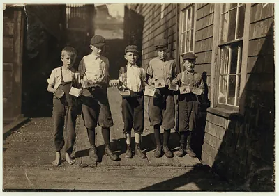 Five boys holding tobacco tags outside a wooden building