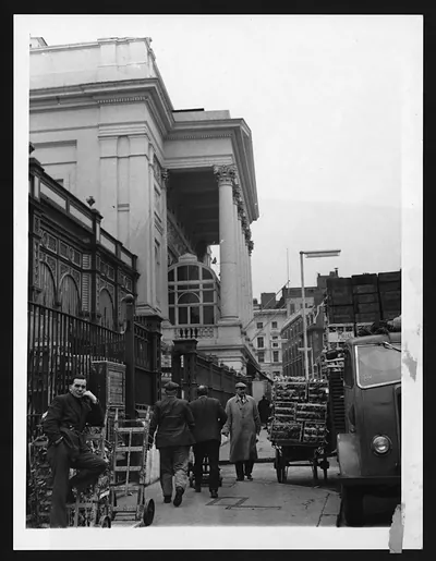 Market street beside a classical building, with crates and a van