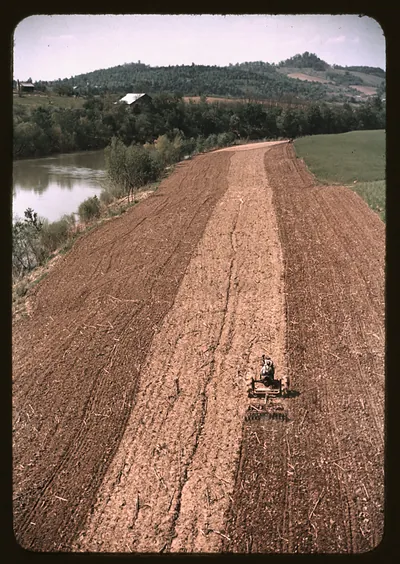 Tractor working a plowed field beside a river