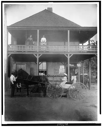 [African Americans and horse-drawn wagon in front of country store, two women stand on balcony]