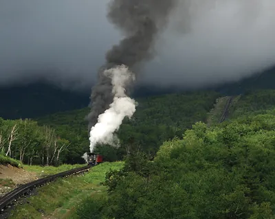 Steam cog train climbing mountainside with smoke plume