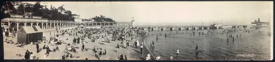 Crowded lakeside beach with bathers, pavilion and steamship