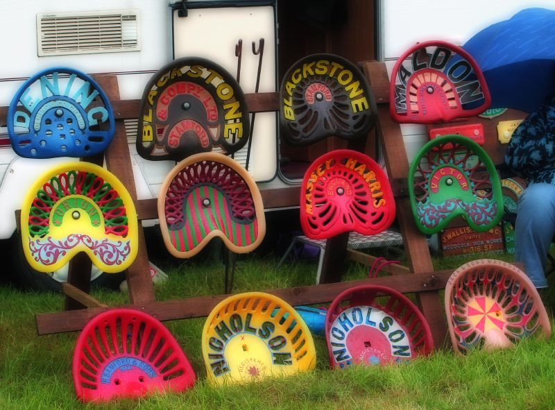 Painted tractor seats displayed on a wooden rack — historic image