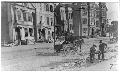 [Two men cleaning street, horse-drawn wagon and damaged buildings in the background, after the 1906 San Francisco earthquake]