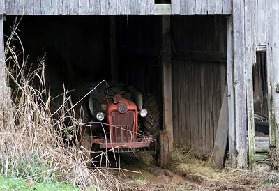 Red vintage tractor parked inside a weathered barn