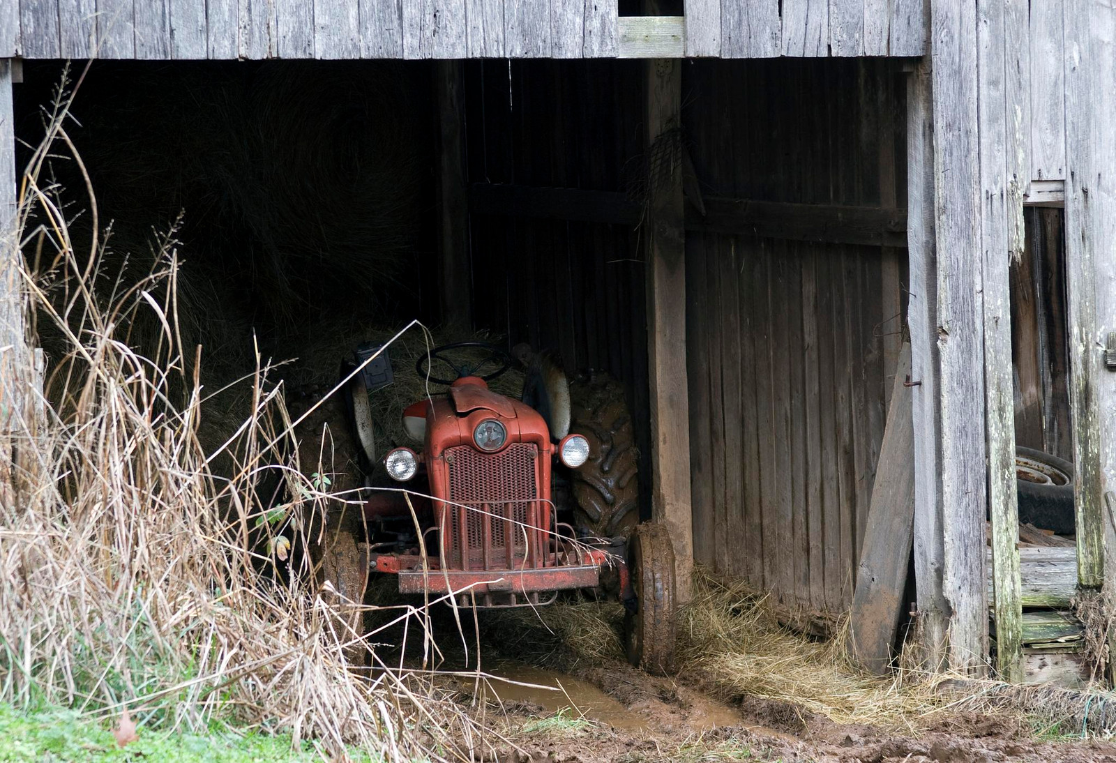 Red vintage tractor parked inside a weathered barn — historic image