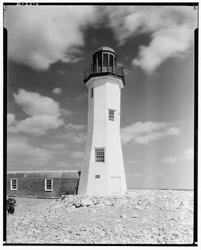 White lighthouse tower beside shingled building on rocky shore