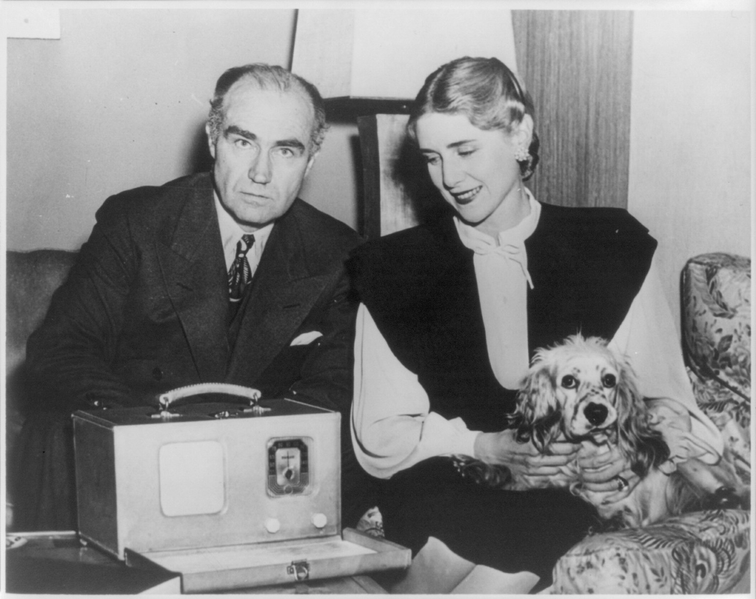 [Henry and Clare Booth Luce on sofa with portable radio and pet cocker spaniel] — historic photograph