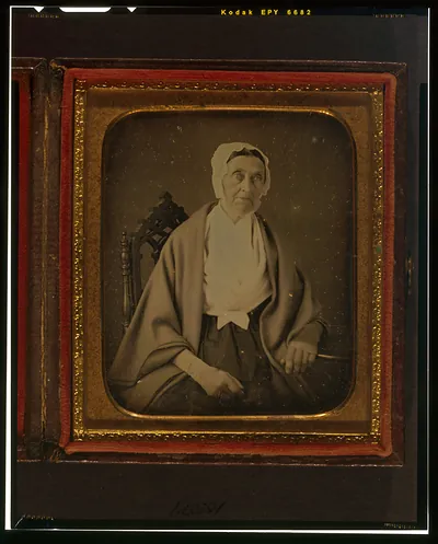 [Unidentified woman seated in chair, with hand resting on table]