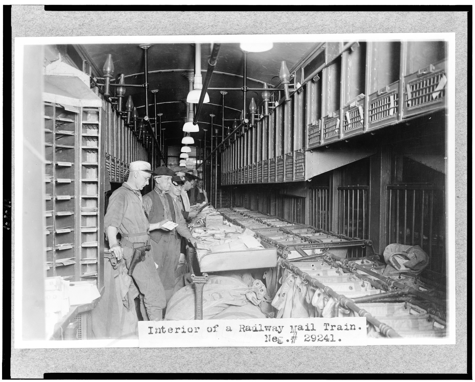 [Men working in a railway mail train], [between 1909 and 1932] — historic photograph