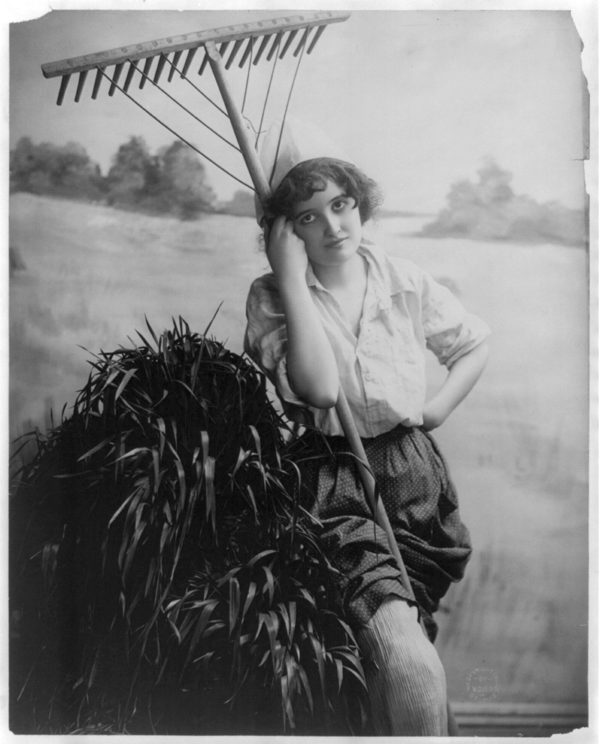 [Young woman modeling: 3/4 lgth., standing, with rake], c1902. — historic photograph