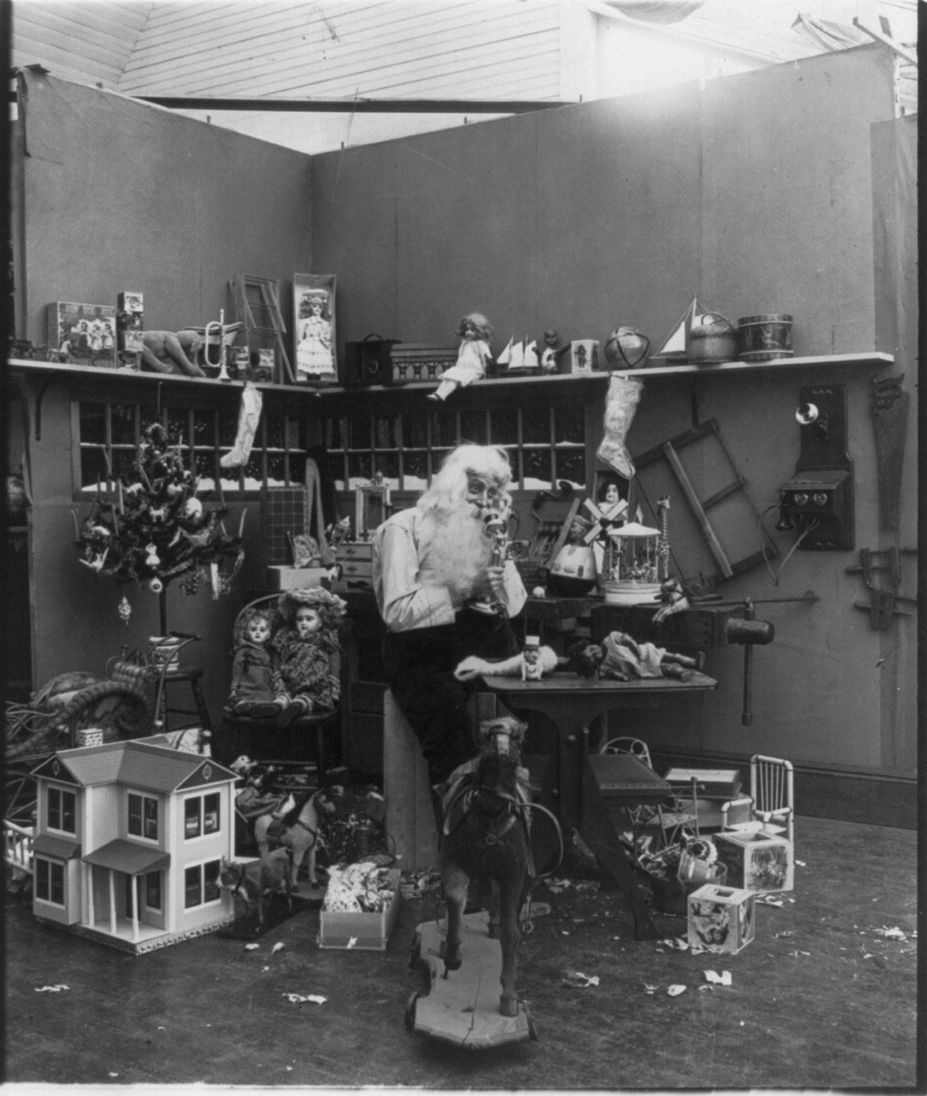 [Santa Claus with children and toys: Santa in his workshop talking on telephone and surrounded by toys], c1906. — historic photograph