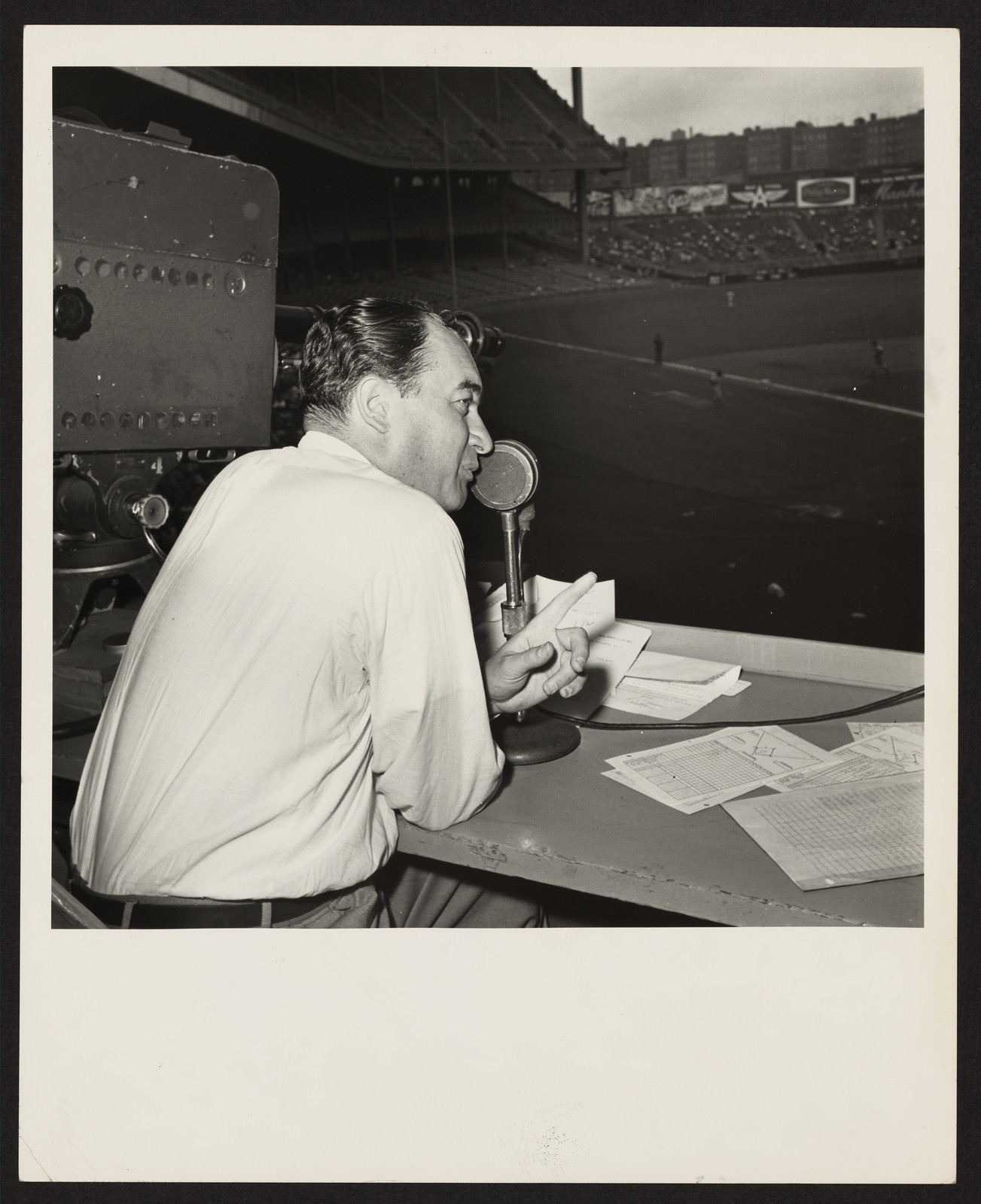 Broadcaster at microphone in a baseball stadium booth — historic image