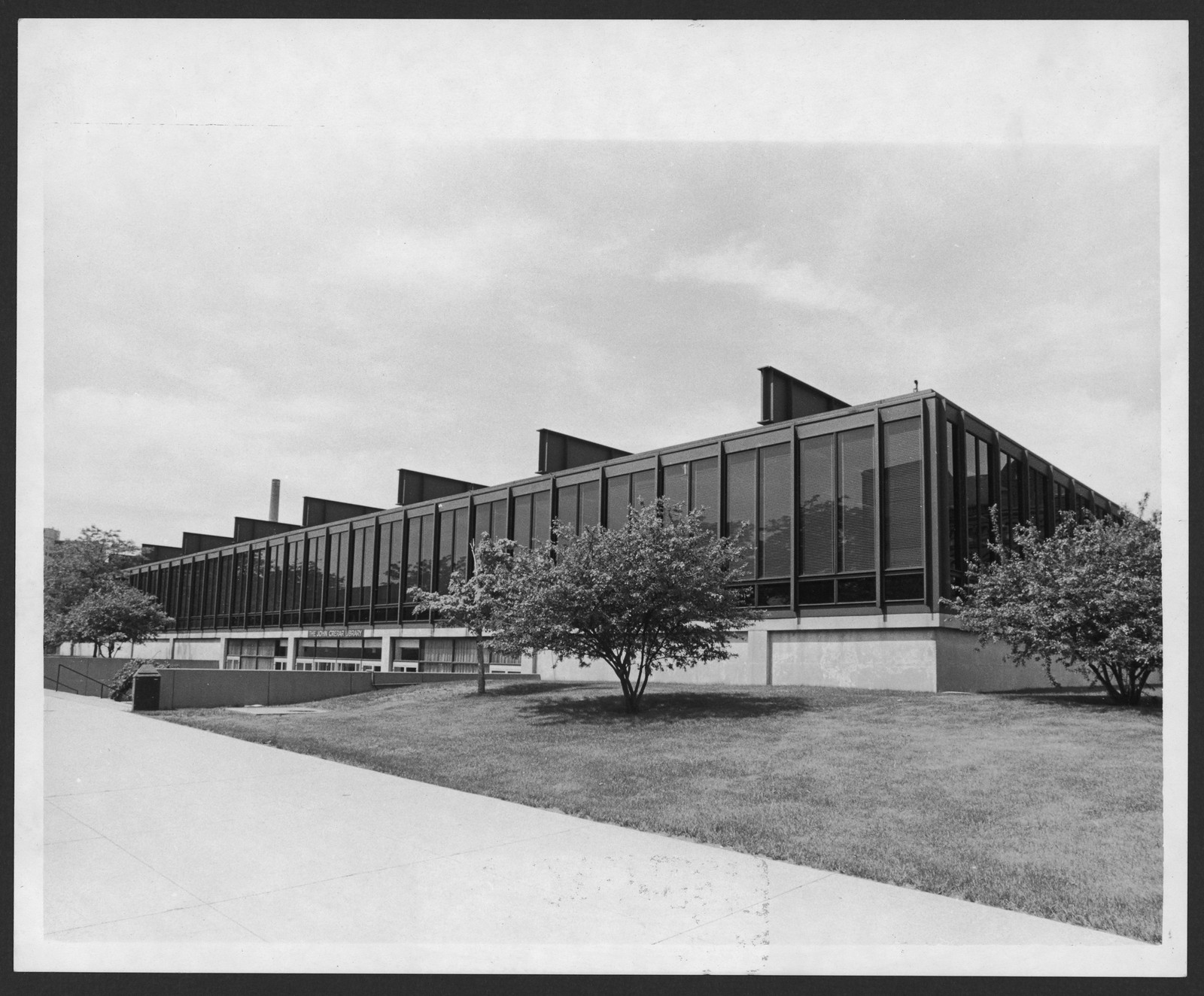 Modernist glass-faced building with lawn and trees, black and white — historic image