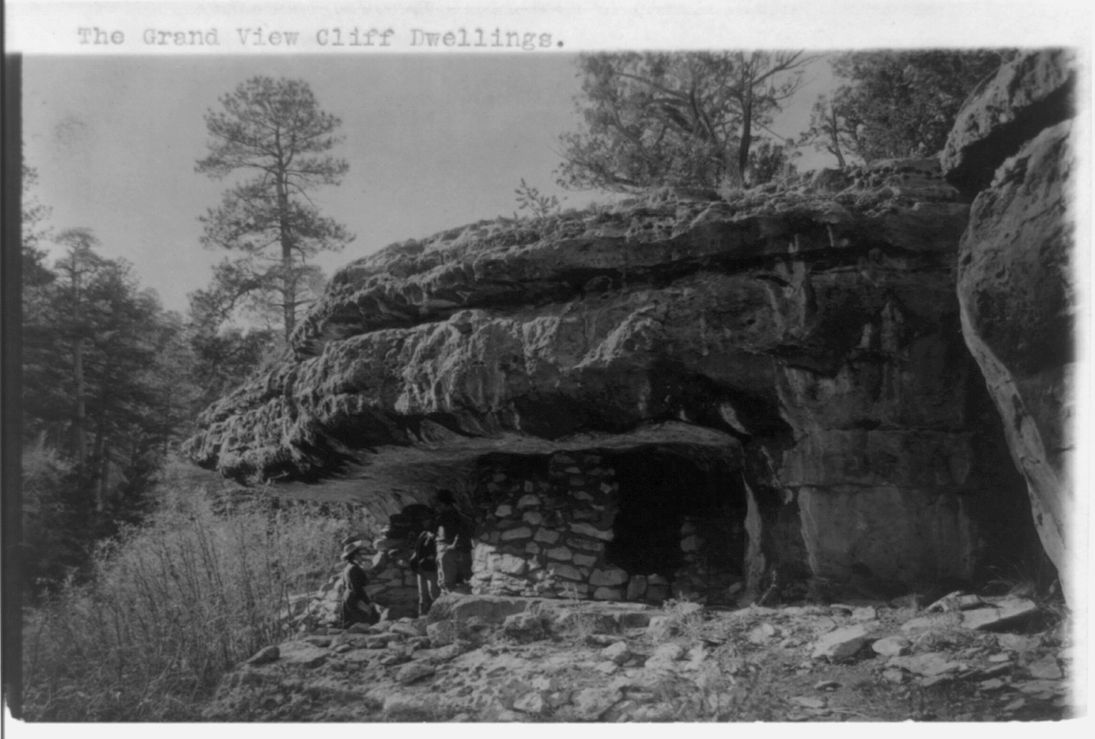 [Grand Canyon and vicinity]: The grand view cliff dwellings [and 3 people], c1906. — historic photograph